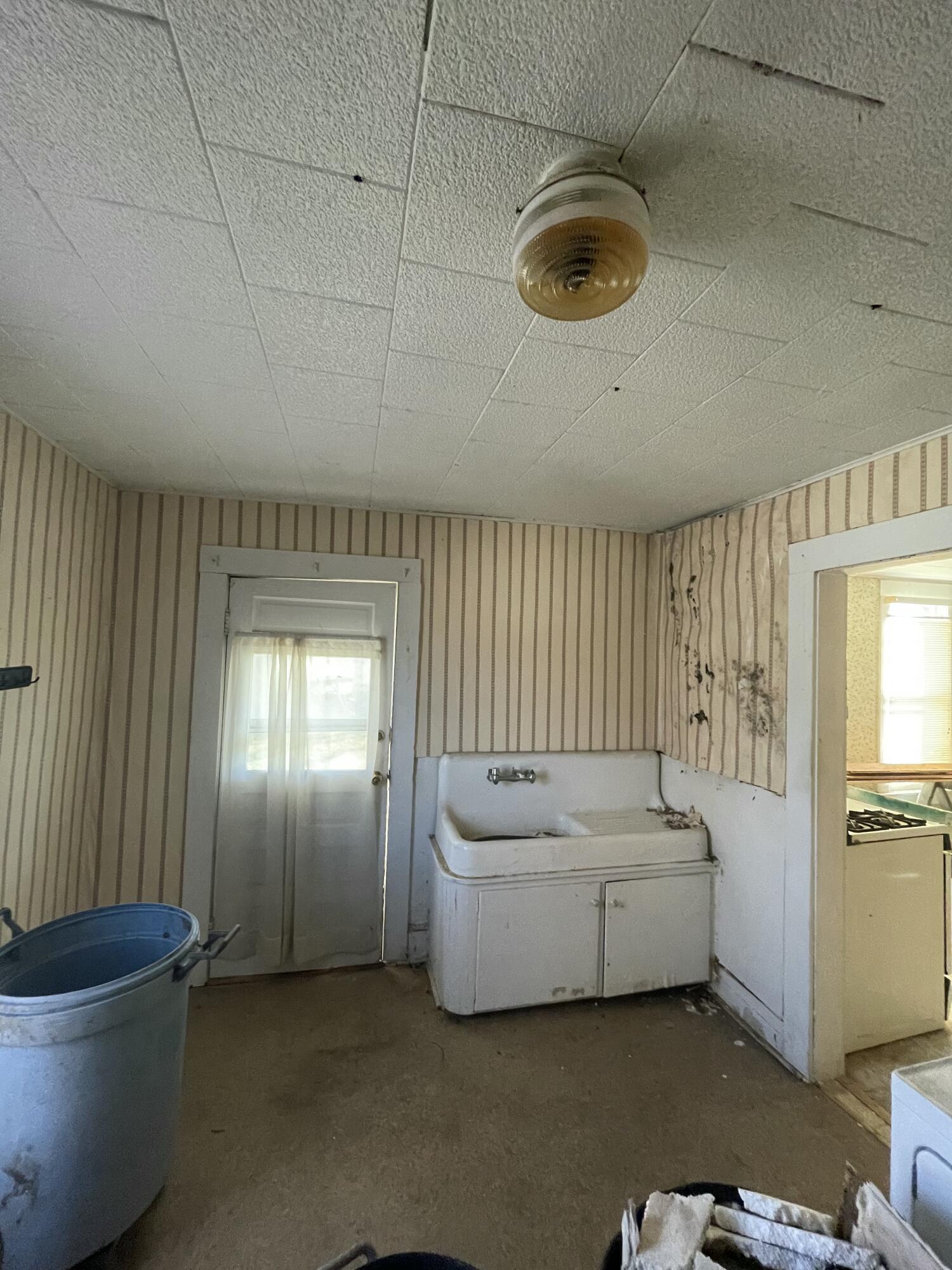 Utility room with a freestanding sink, striped wallpaper, and damaged walls.