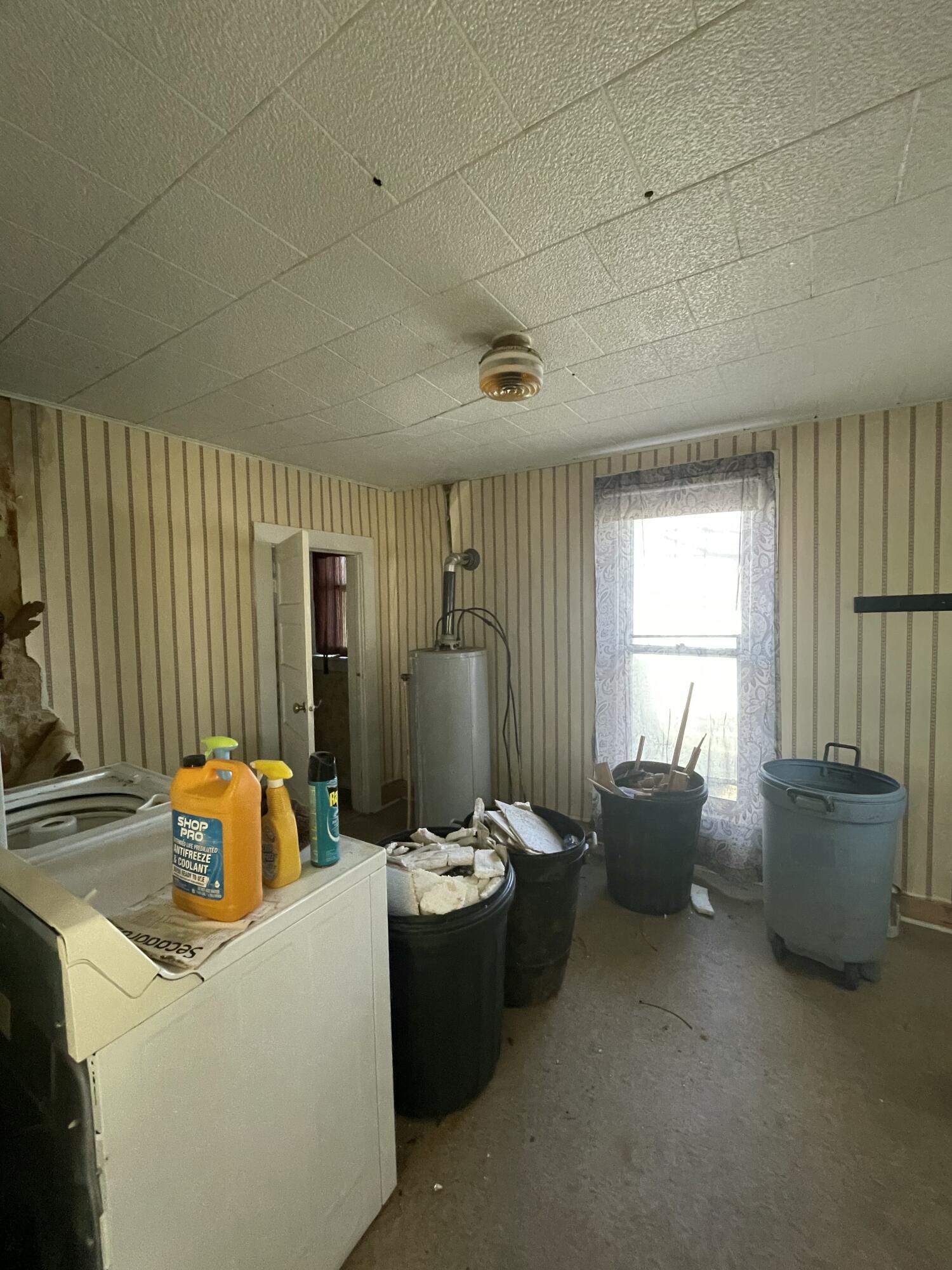 Cluttered laundry room with a washing machine, water heater, and bins of debris.