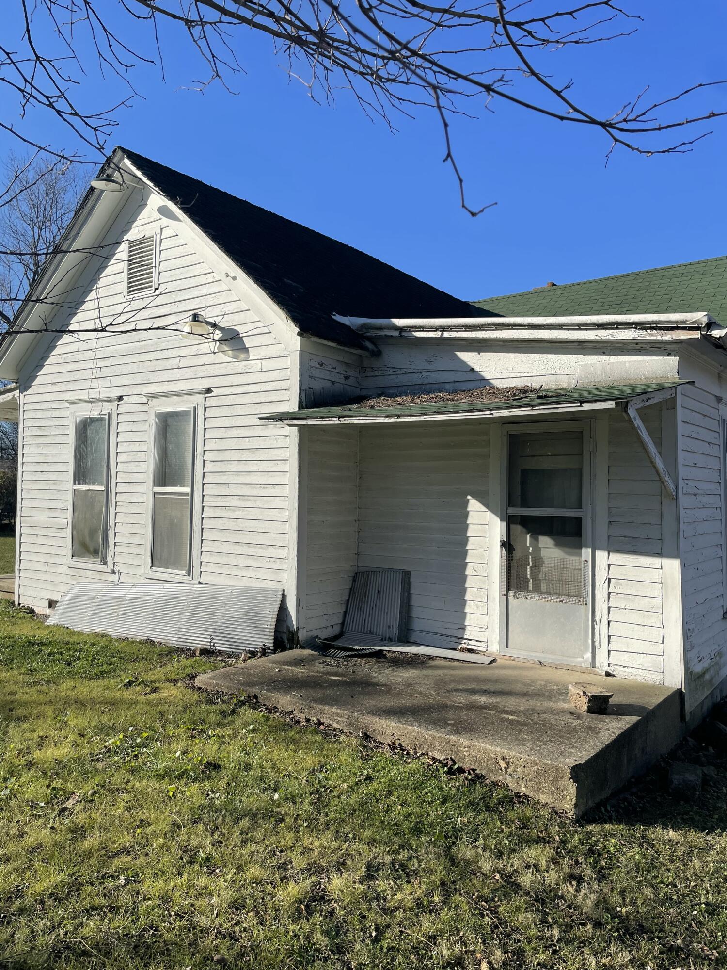 Weathered white clapboard house with a covered side entrance and screen door.