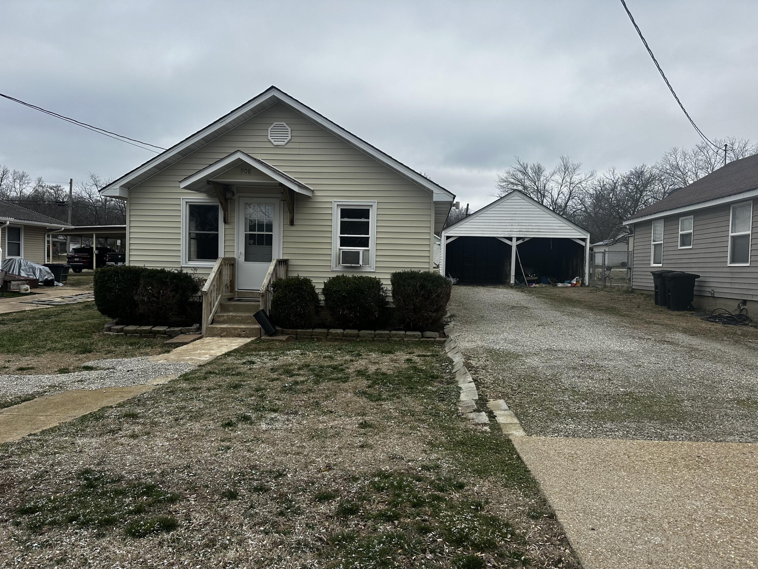 Single-story house with a covered entry, gravel driveway, and detached carport.