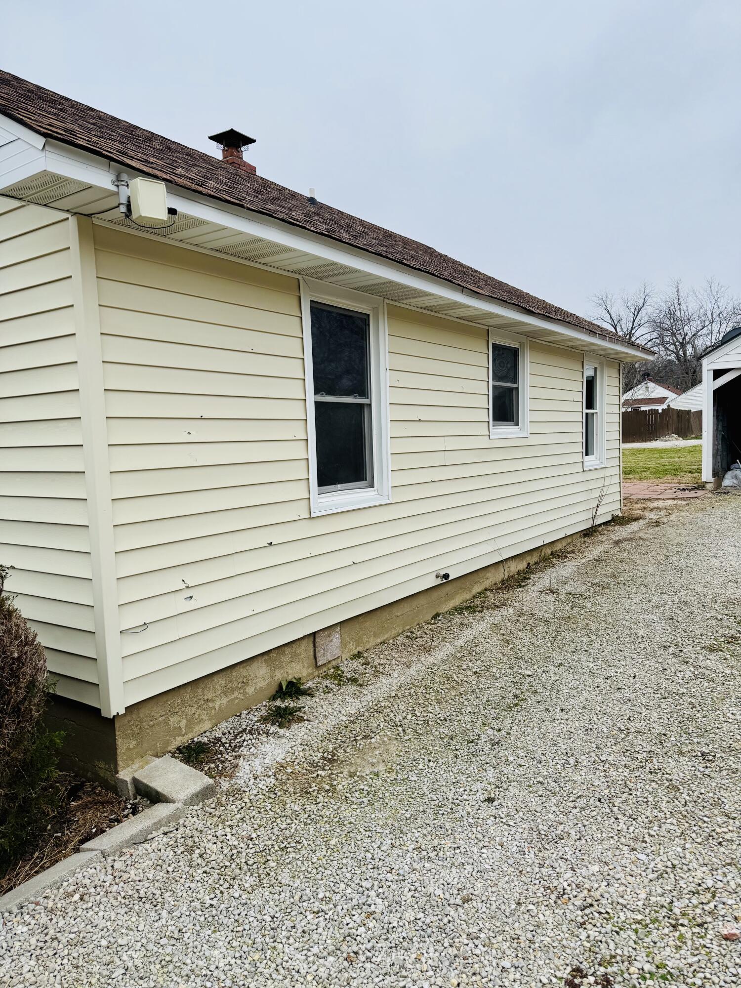 Side of a pale yellow house with white-trimmed windows beside a gravel driveway.