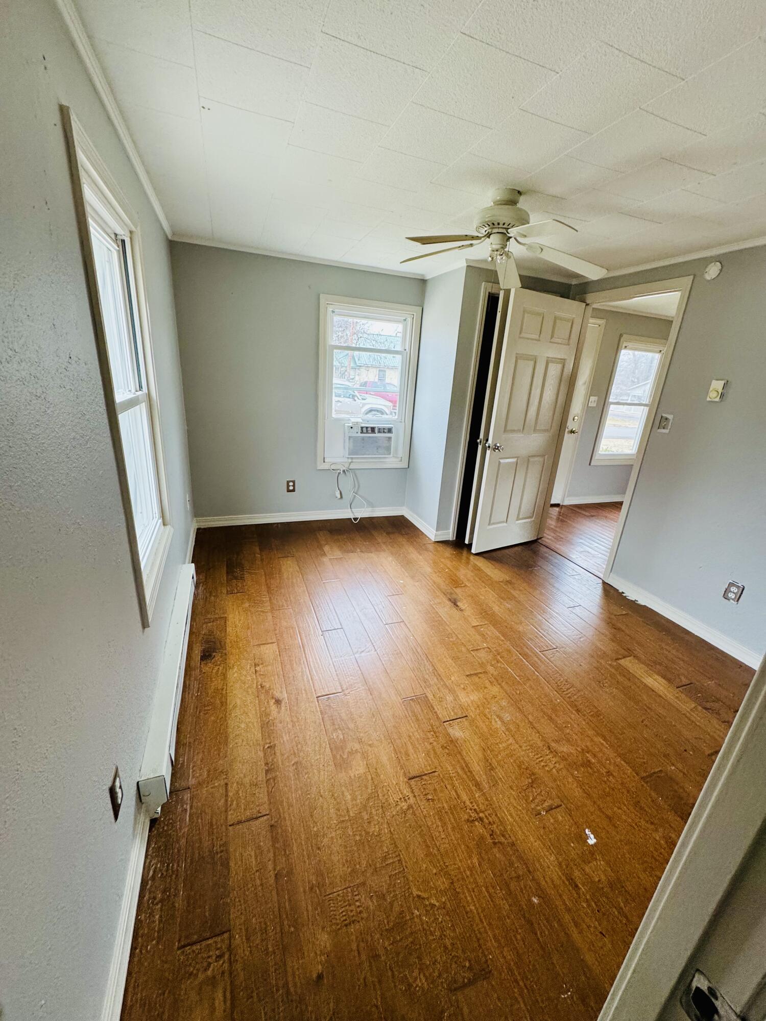 Empty room with worn hardwood floors, a ceiling fan, and a window air conditioner.