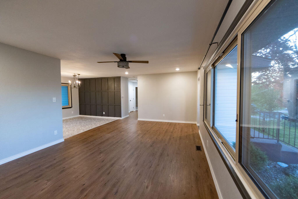 Empty living and dining area with wood-look floors, large windows, and a dark paneled accent wall.