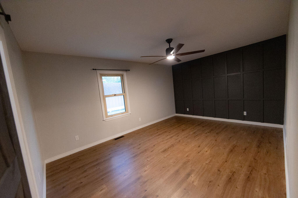 Empty room with wood-look flooring, a dark paneled accent wall, and a ceiling fan.
