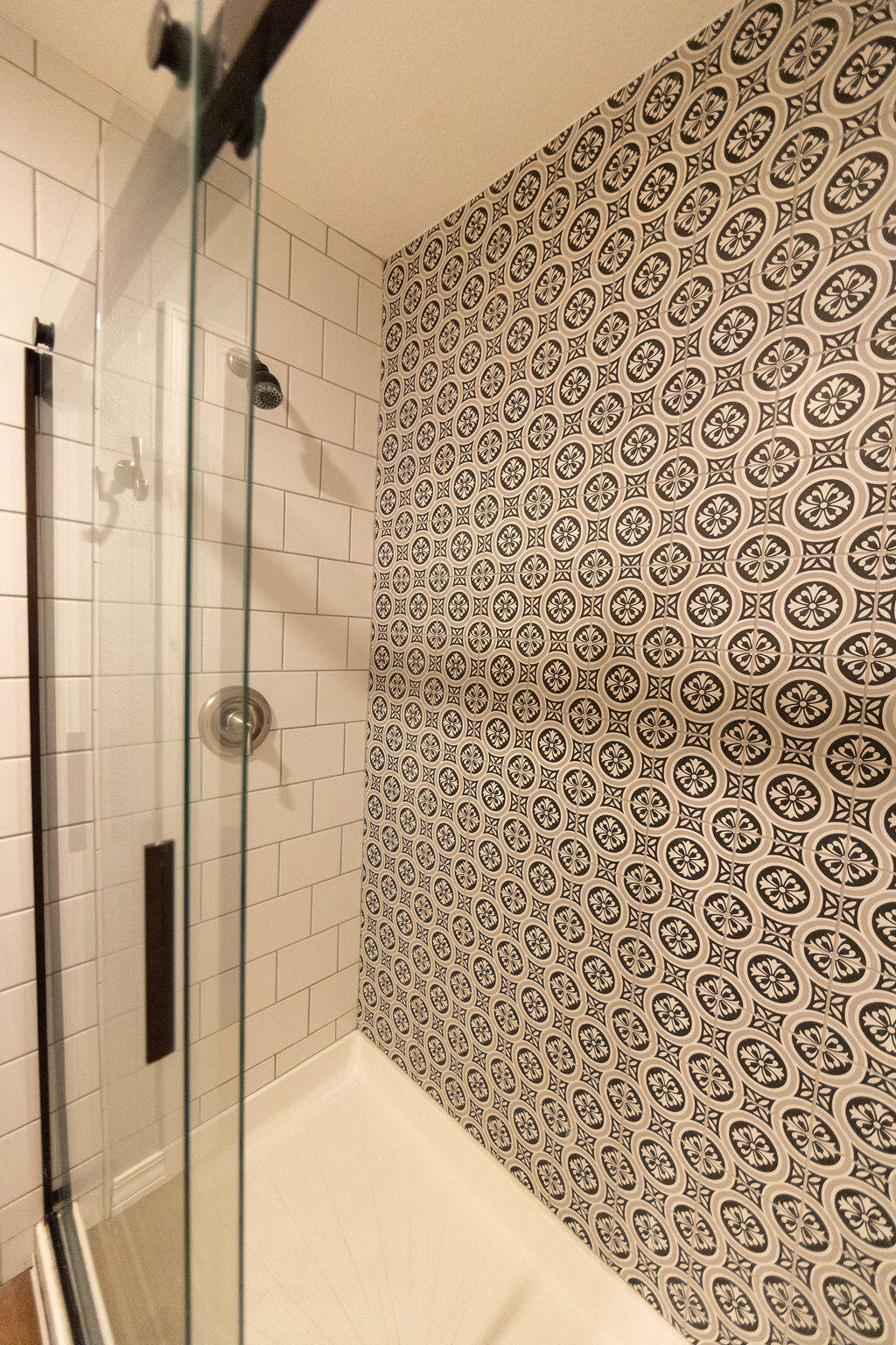 Walk-in shower with glass doors and a distinctive black-and-cream patterned tile wall.