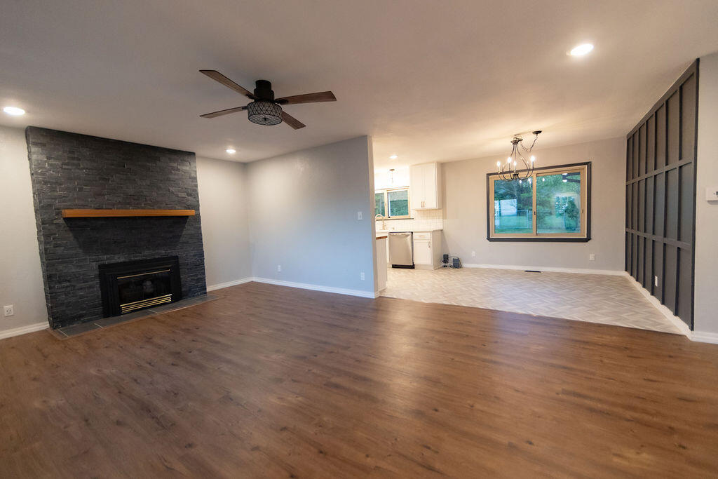 Open living room with stone fireplace, wood flooring, and adjoining dining area.