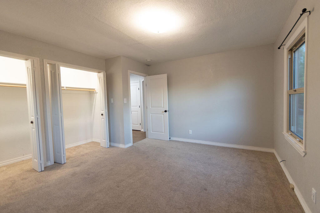 Empty bedroom with beige carpet, two open closets, and a window.