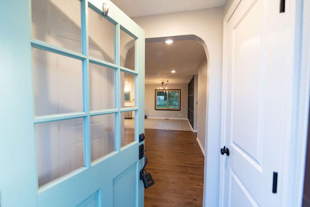Open turquoise front door reveals a wood-floored hallway and arched opening into a bright room.