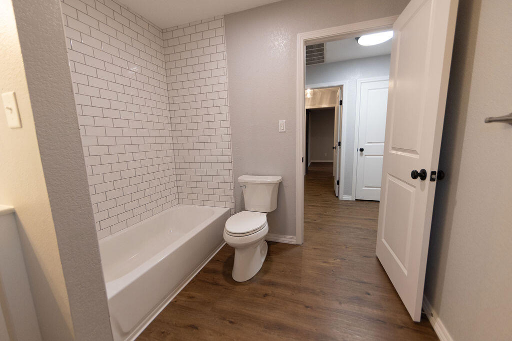 Bathroom with a subway-tile tub surround, toilet, and wood-look flooring.
