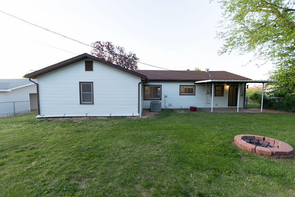 Rear of a single-story house with a covered patio, grassy yard, and circular brick fire pit.