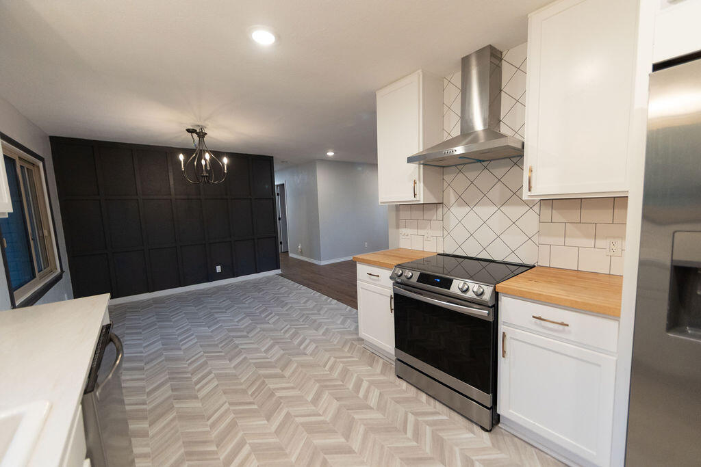 Kitchen with white cabinets, stainless steel range, wood countertops, and a dark paneled dining-area wall.