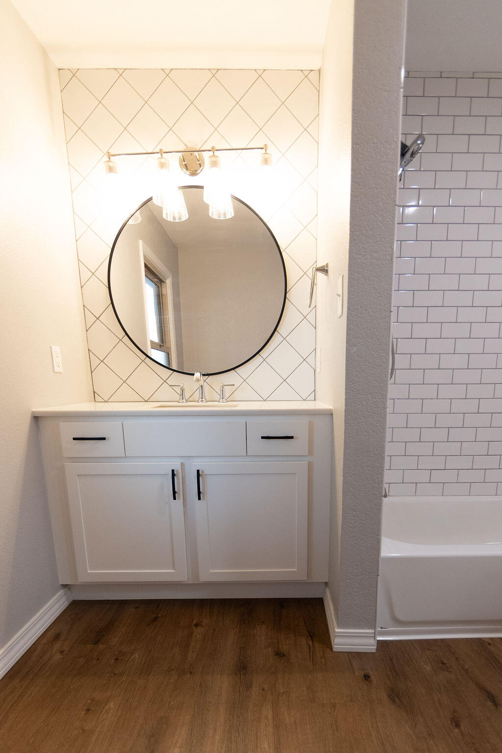 Bathroom with a white vanity, round mirror, diagonal tile backsplash, and subway-tile tub surround.