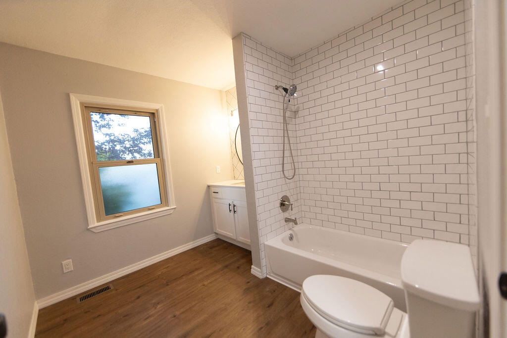 Bathroom with a subway-tile tub and shower, frosted window, and wood-look flooring.