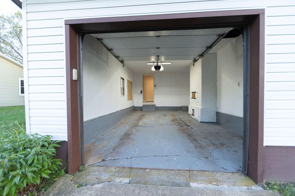 Open attached garage with white walls, a concrete floor, and a door at the back.