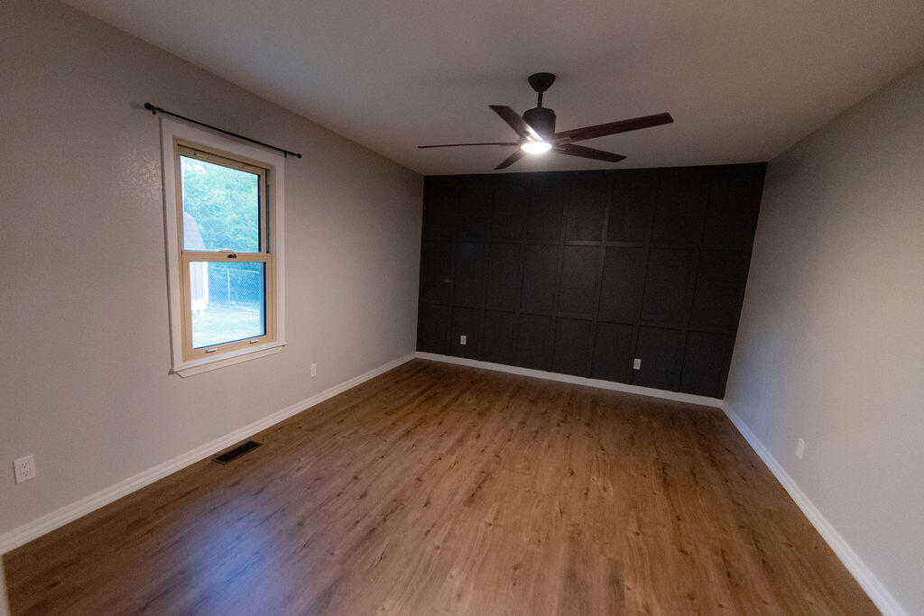 Empty room with wood-look flooring, a dark paneled accent wall, and a ceiling fan.