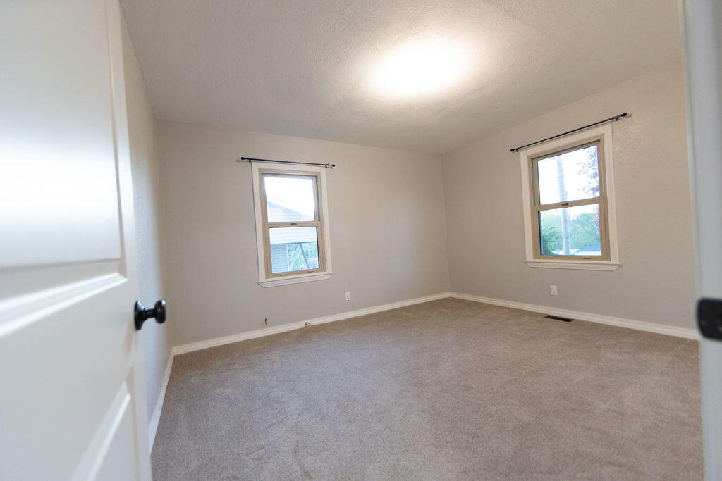 Vacant bedroom with beige carpet, two windows, and a ceiling light.