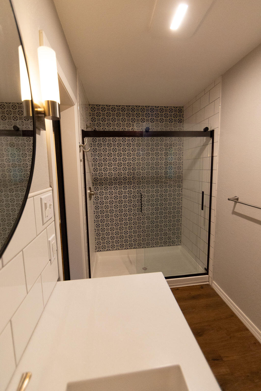 Bathroom with a glass shower, patterned tile accent wall, and white vanity.