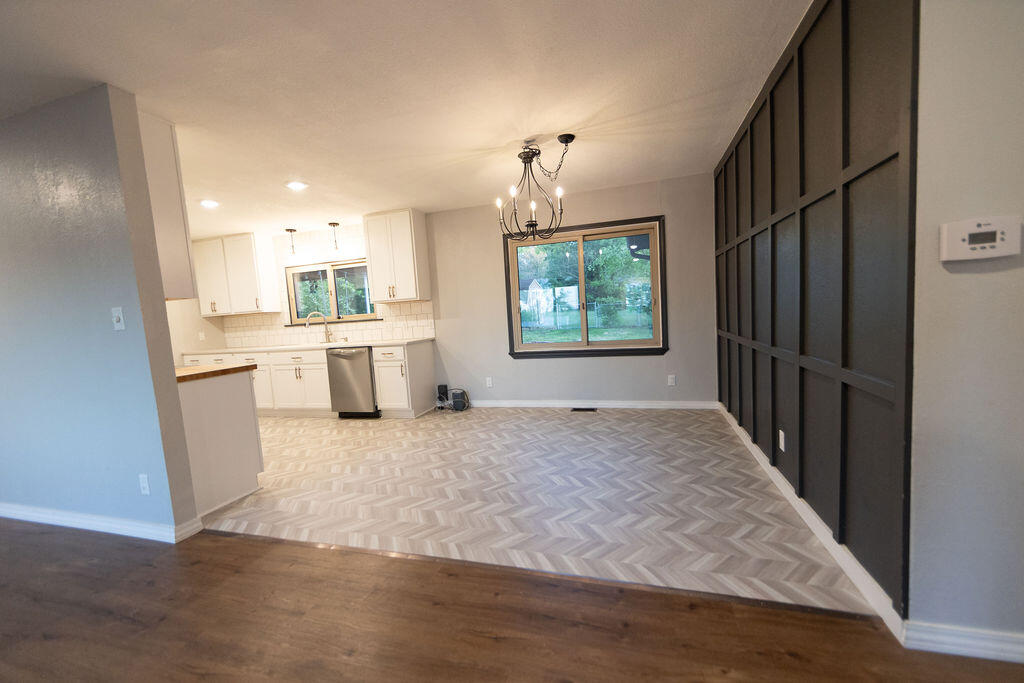 Open dining area and kitchen with herringbone flooring, a chandelier, and black grid partition.