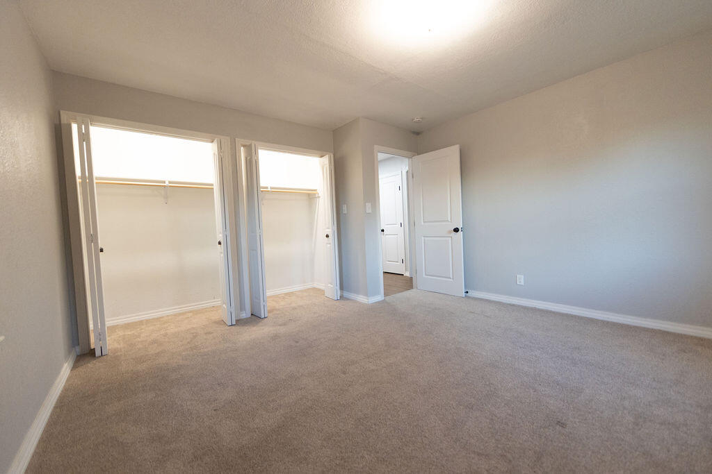 Vacant bedroom with beige carpet and two open closets.