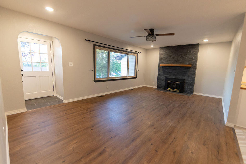 Unfurnished living room with wood-look floors, a large window, and a dark stone fireplace.