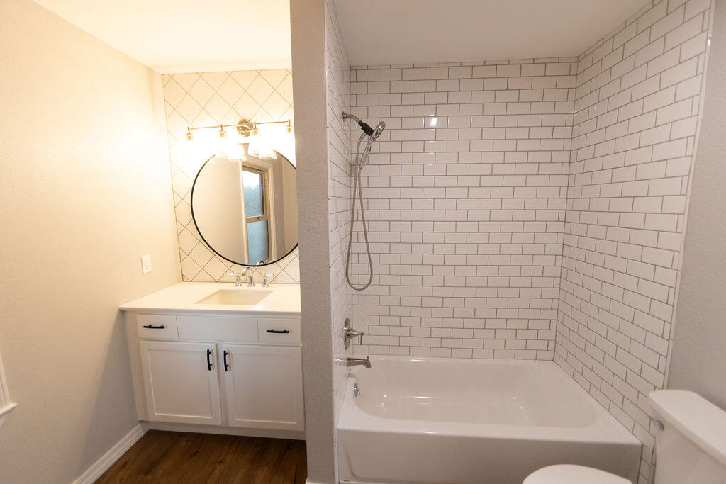 Bathroom with a white subway-tiled tub and shower beside a vanity with a round mirror.