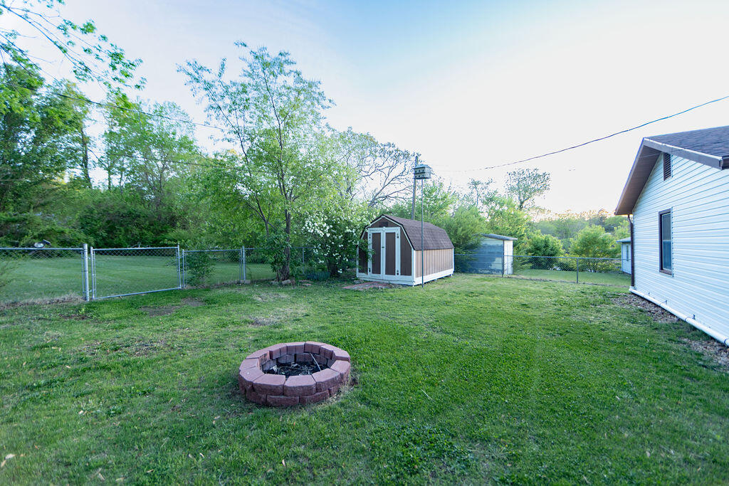 Backyard with a circular stone fire pit, storage shed, and chain-link fencing.