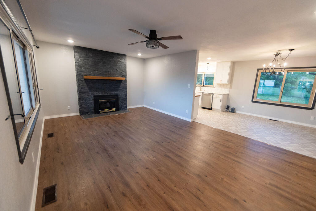 Open living room with wood-look floors, dark stone fireplace, ceiling fan, and adjoining dining area.