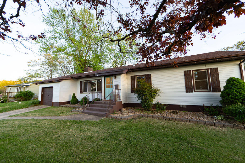 Single-story white home with an attached garage, front steps, and mature trees framing the lawn.