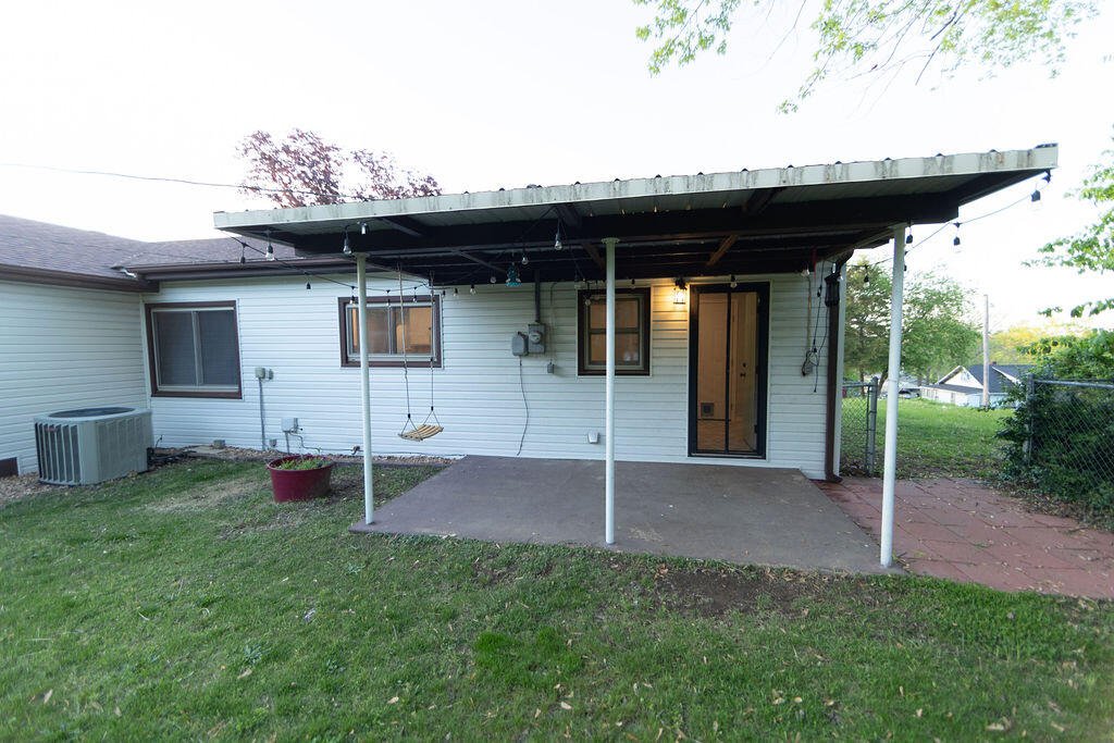 Rear of a single-story home with a broad metal patio canopy and grassy yard.