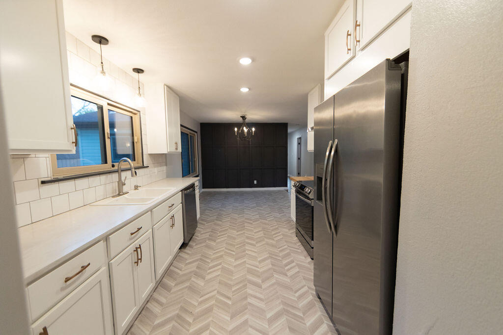 Galley kitchen with white cabinets, stainless steel appliances, and gray chevron-pattern flooring.