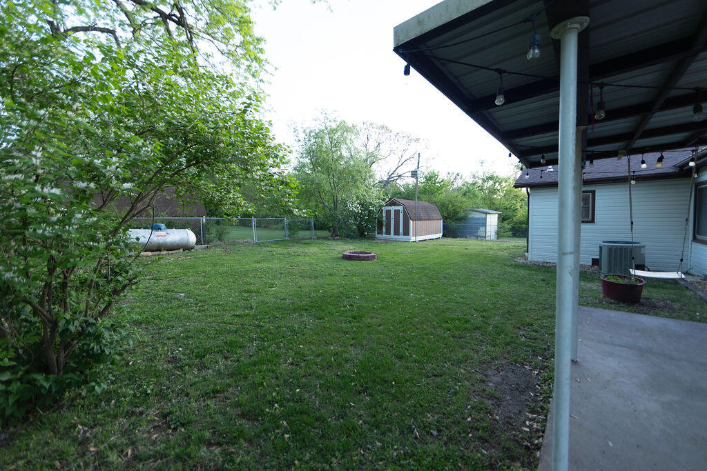 Backyard with a covered patio, leafy trees, storage shed, propane tank, and fire pit.