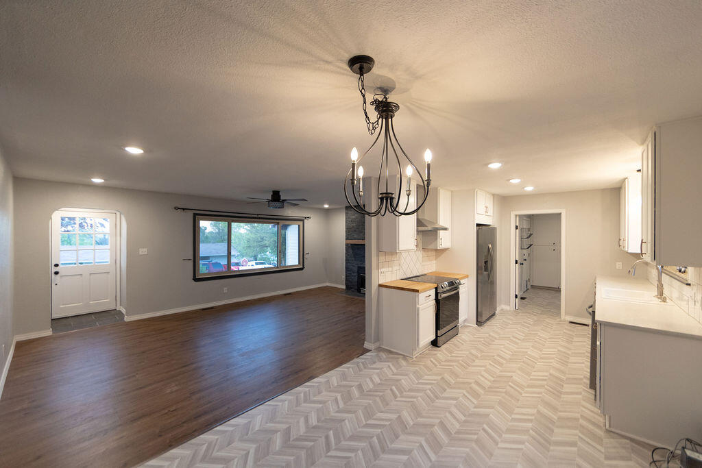 Open-plan kitchen and living area with white cabinets, stainless steel appliances, and contrasting wood and patterned floors.