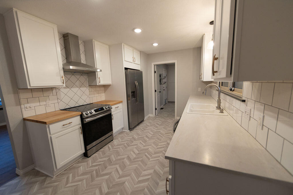 Galley kitchen with white cabinets, stainless steel appliances, and a gray herringbone floor.