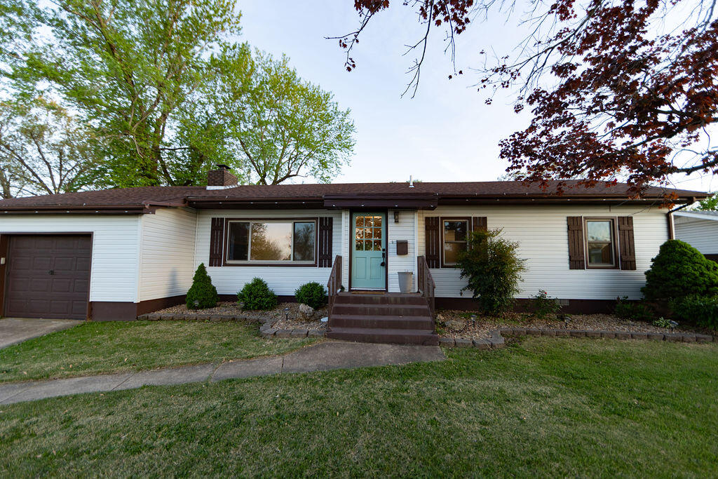 Single-story white ranch house with an attached garage, blue front door, and lawn.