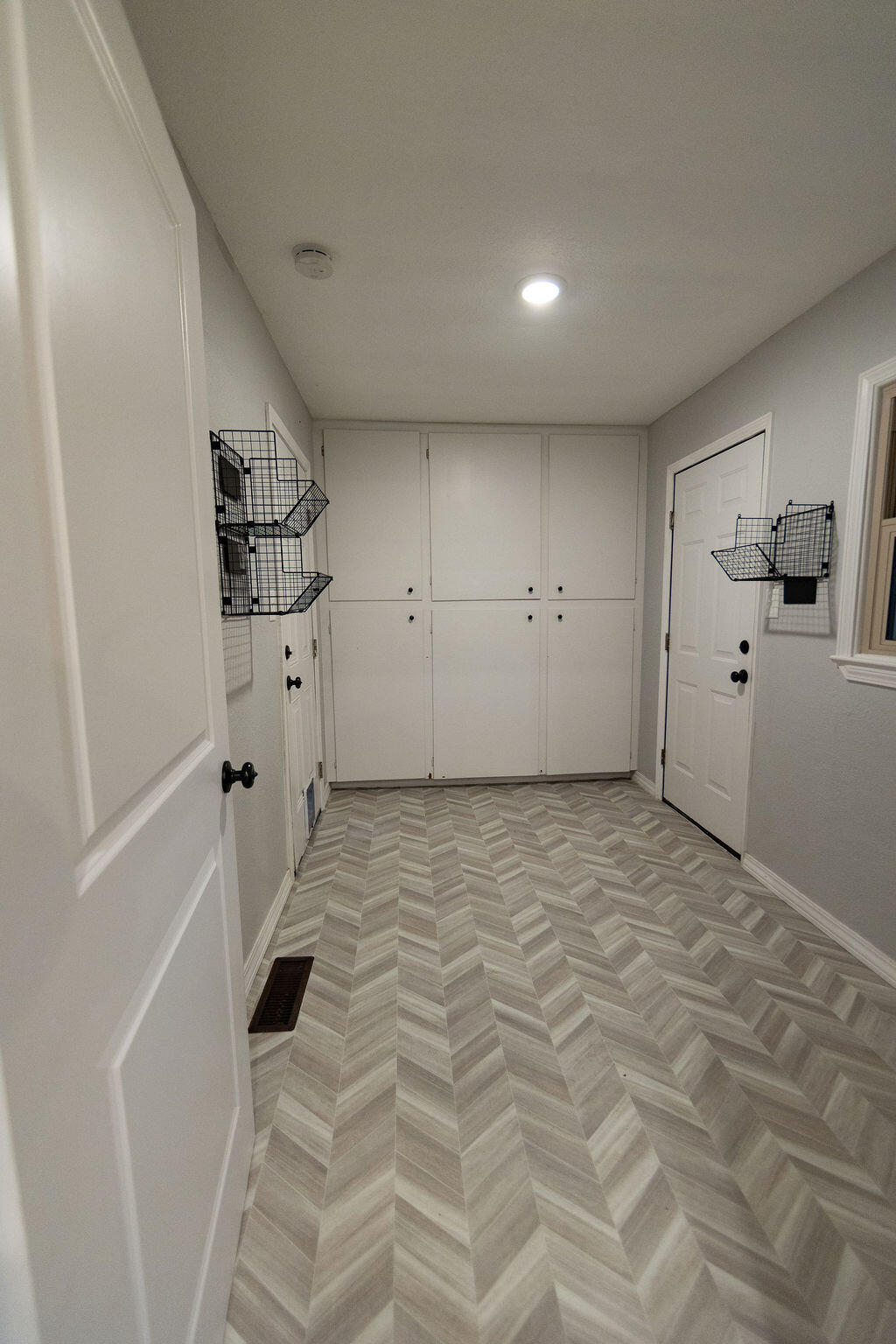 Entryway with built-in cabinets, wire baskets, and herringbone-pattern flooring.