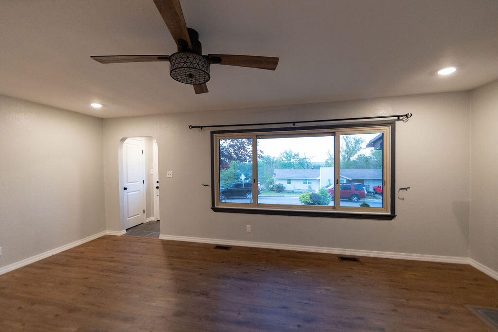 Empty room with wood flooring, a ceiling fan, and a large street-facing window.