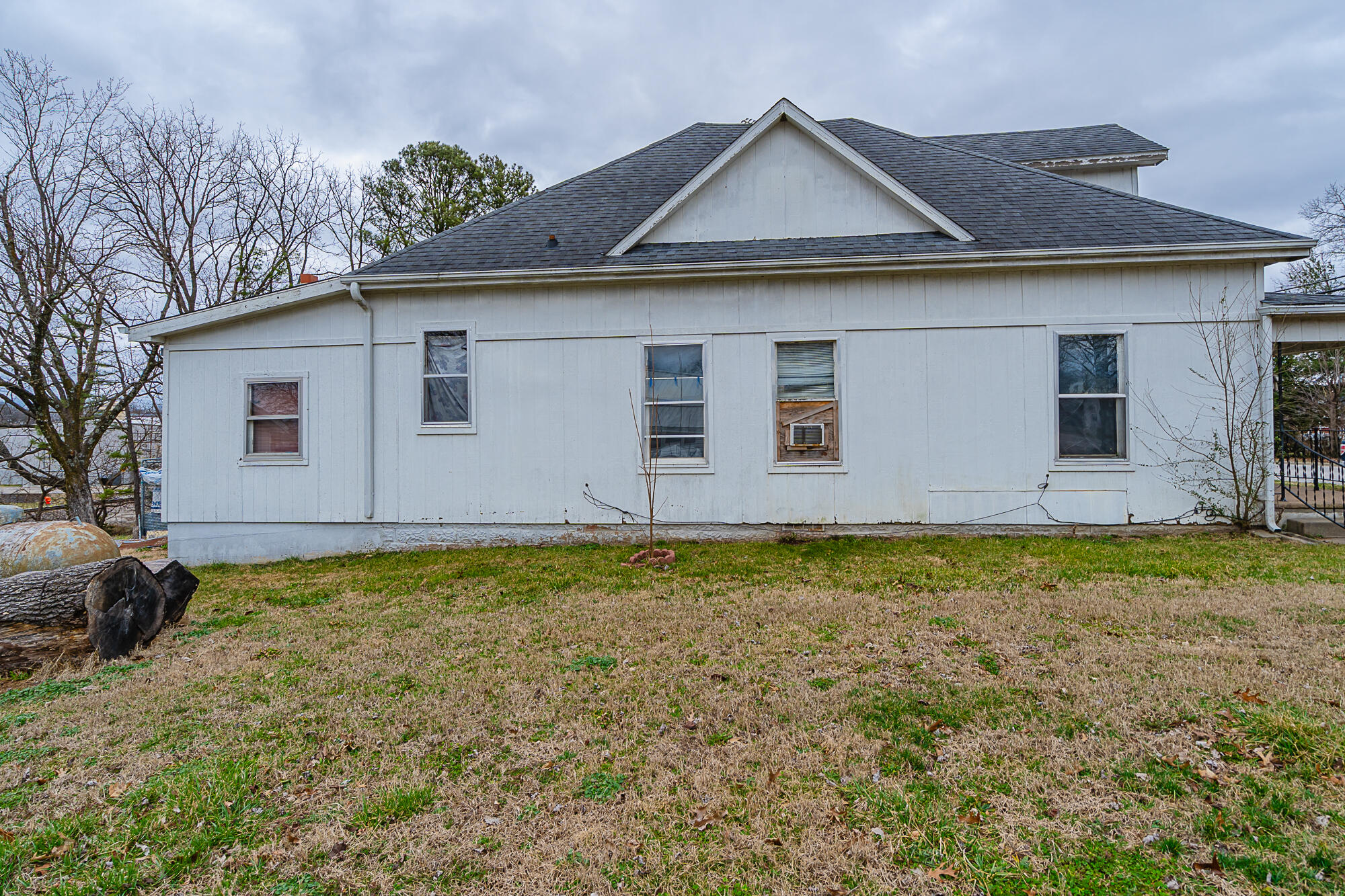 White-sided house with dark shingle roof and dormant lawn, viewed from the side.