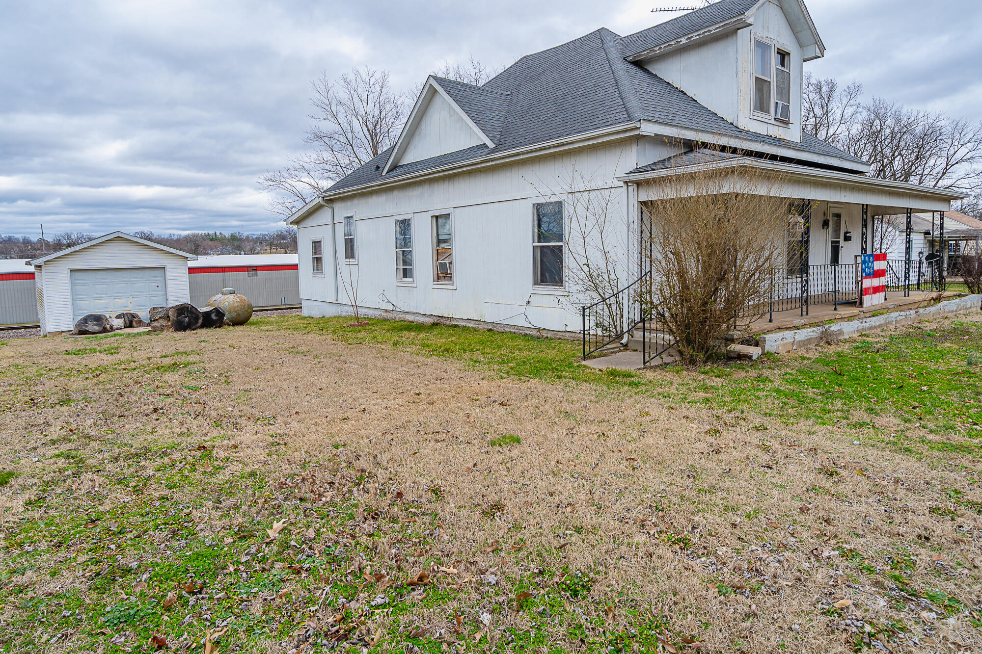 White two-story house with a covered porch, detached garage, and railroad tracks behind the lawn.