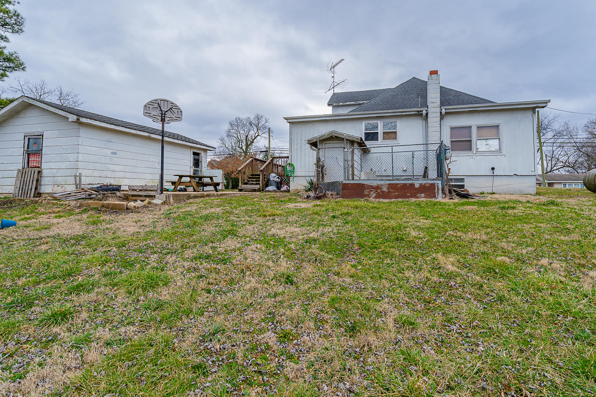 Rear of a white house with a fenced patio, detached outbuilding, and basketball hoop in the yard.