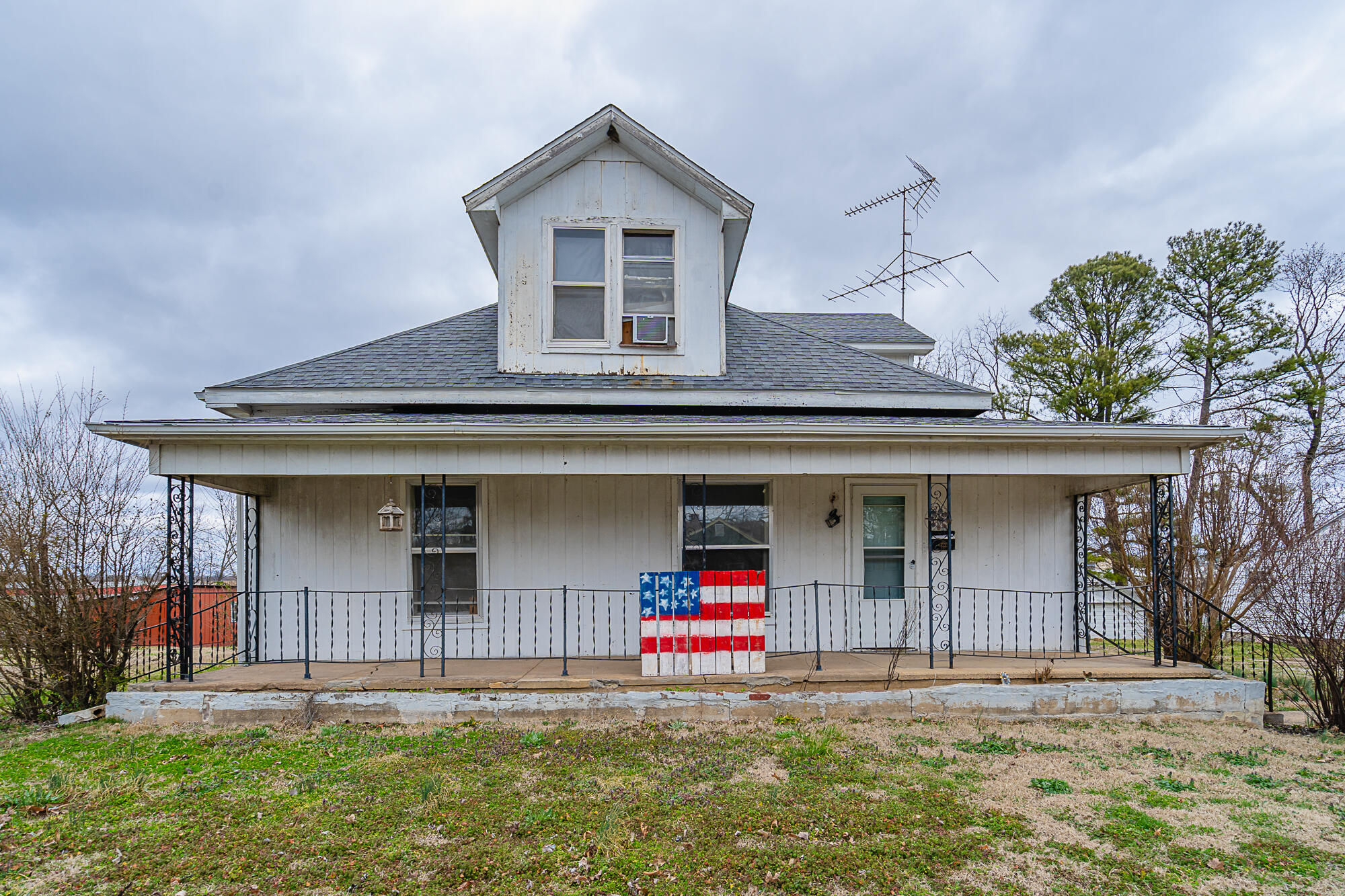 White two-story house with a broad covered porch and an American flag panel by the railing.