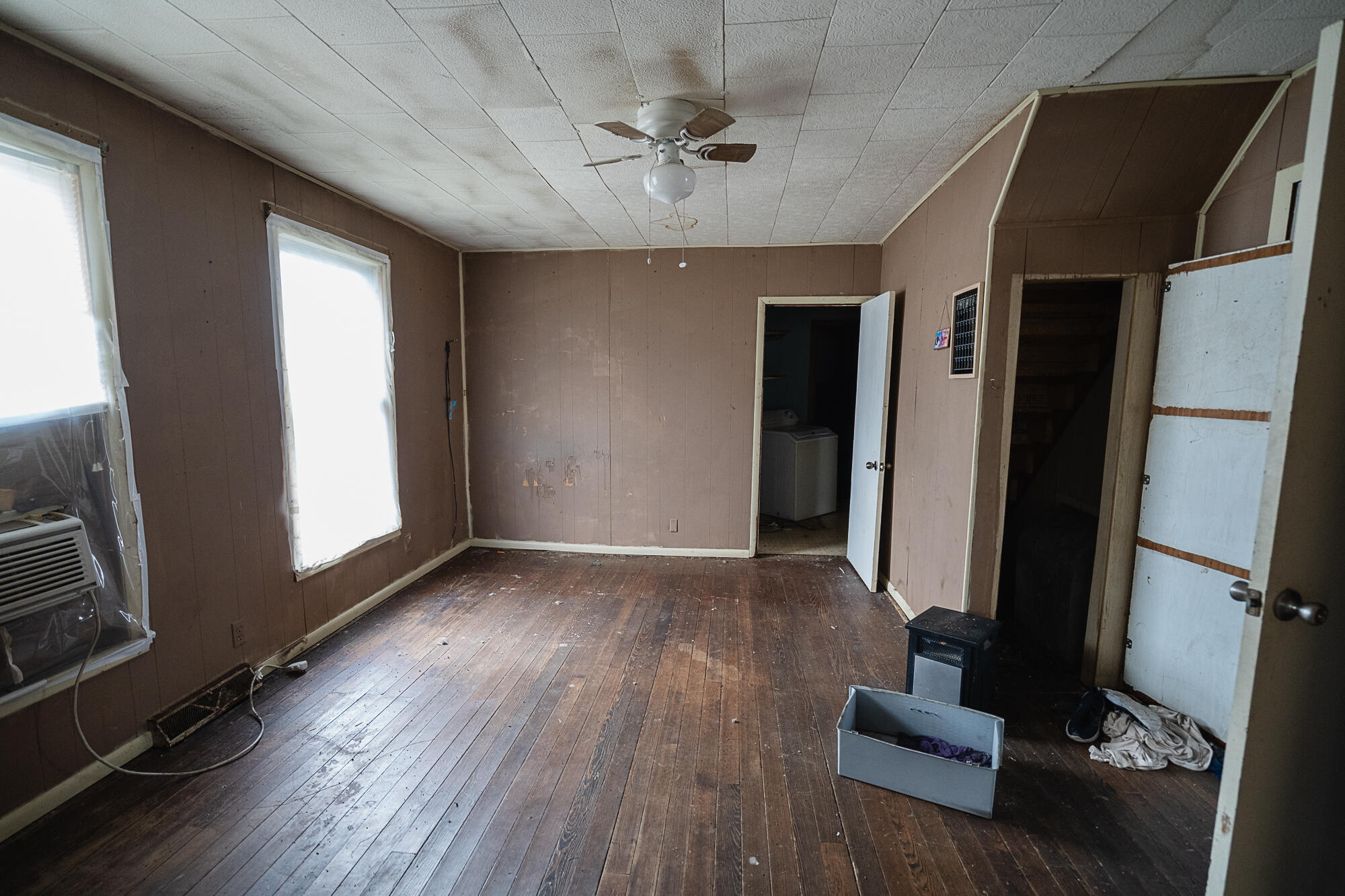 Room with worn wood floors, paneled walls, a ceiling fan, and an open doorway to a washer.