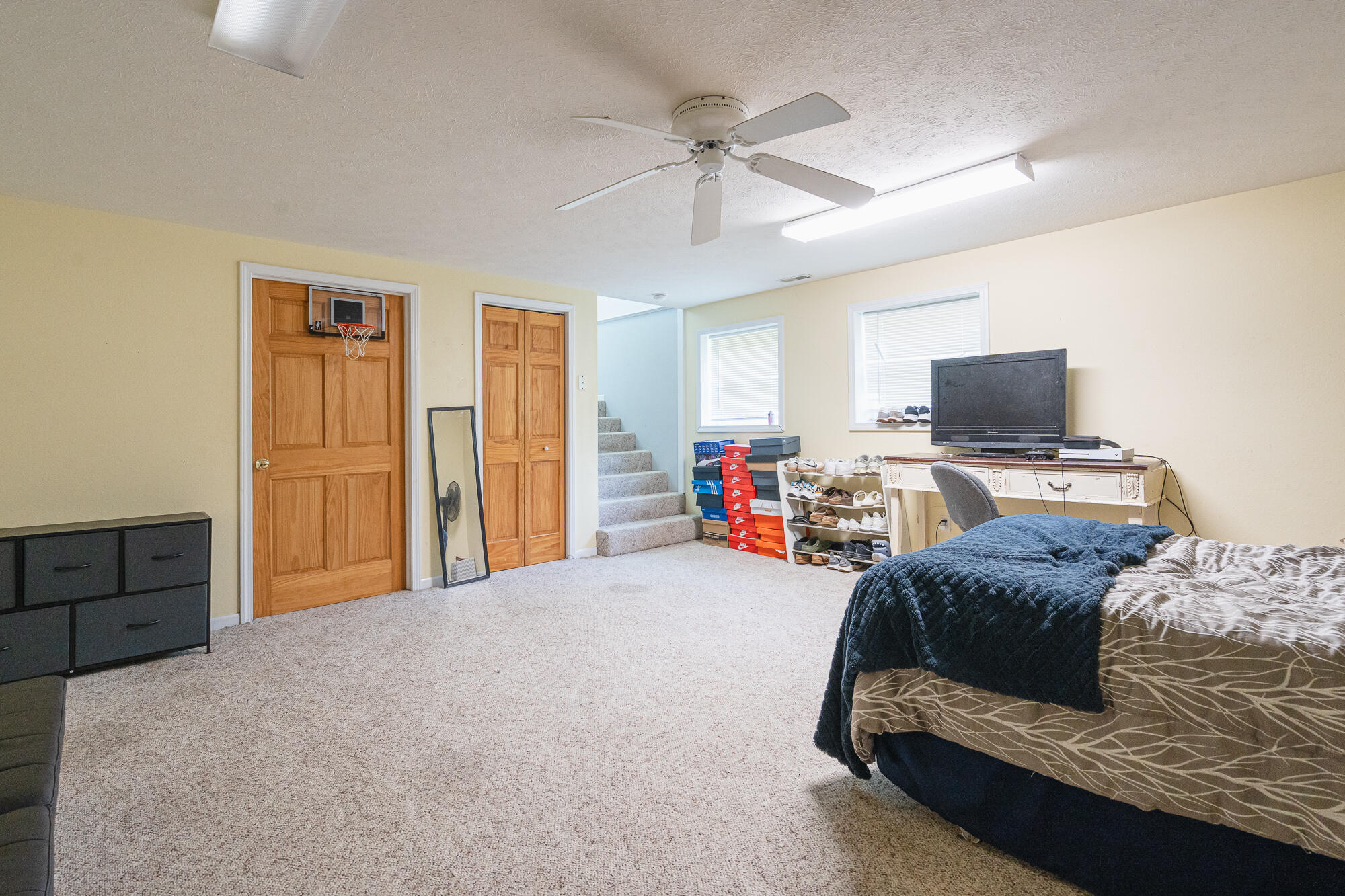 Bedroom with a basketball hoop over the wooden door, carpeted stairs, and a bed beside a television.