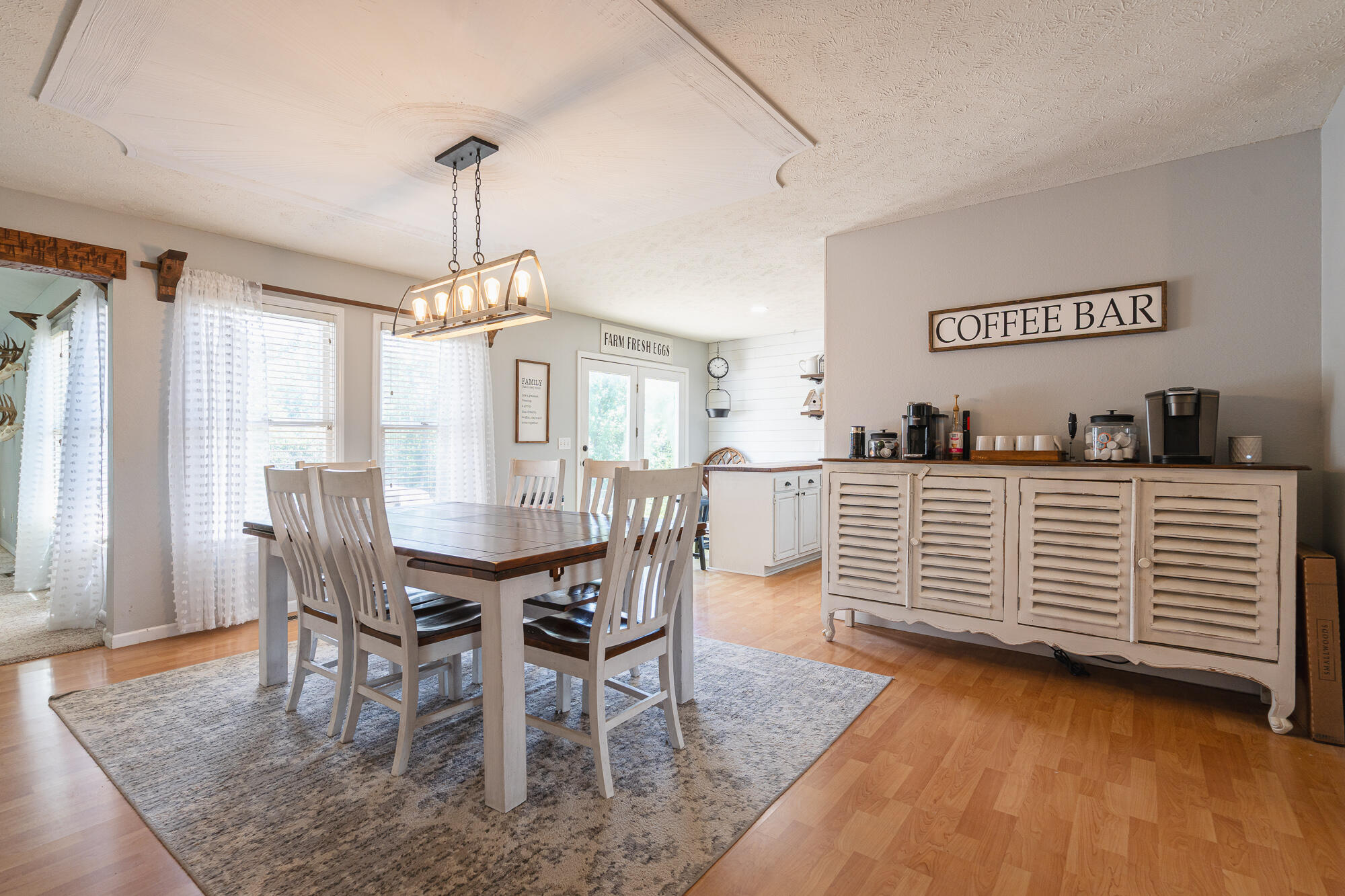 Dining room with white chairs, a large gray rug, and a coffee bar sideboard.