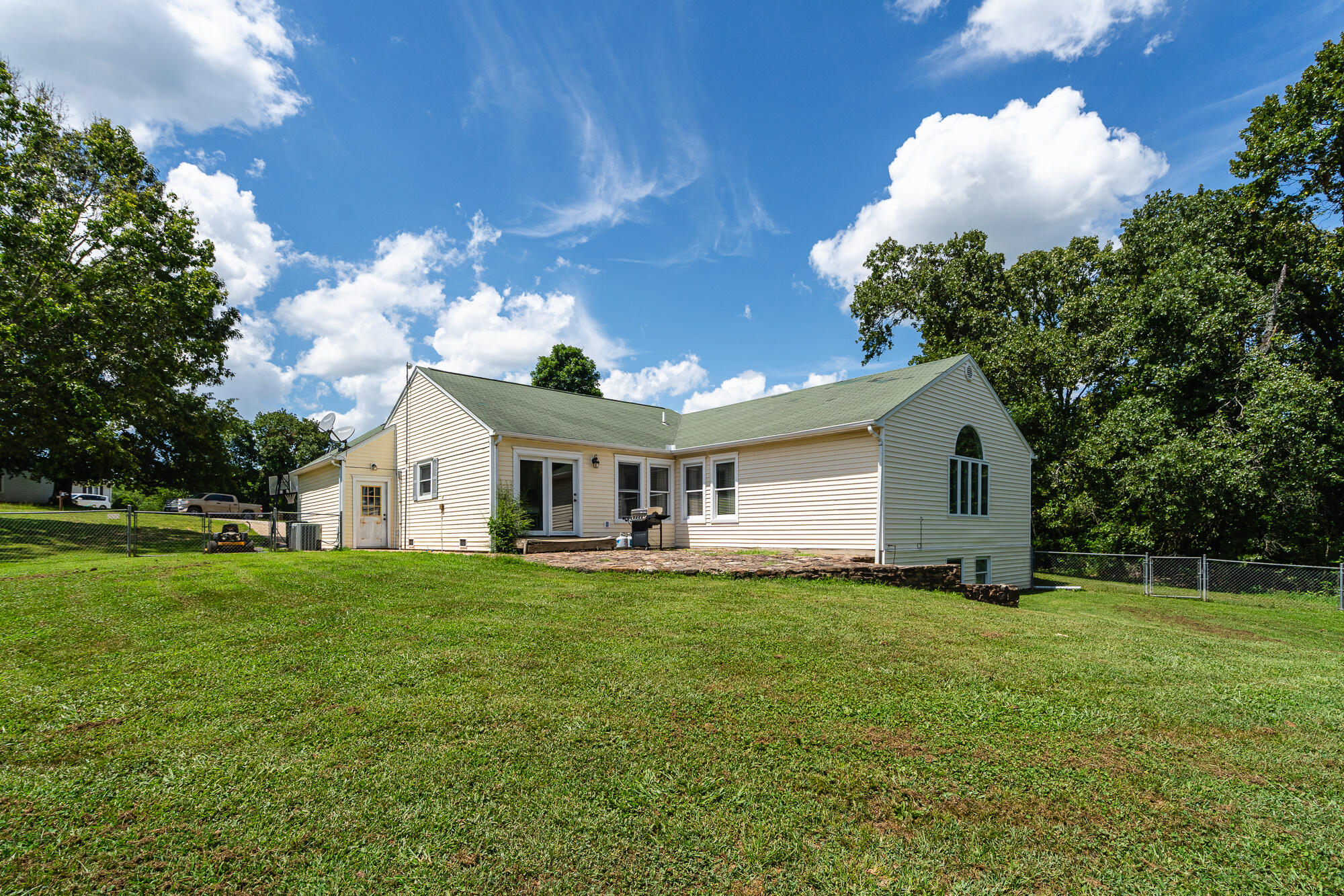 Cream-sided home with green roof, large arched window, and fenced lawn viewed from the rear.