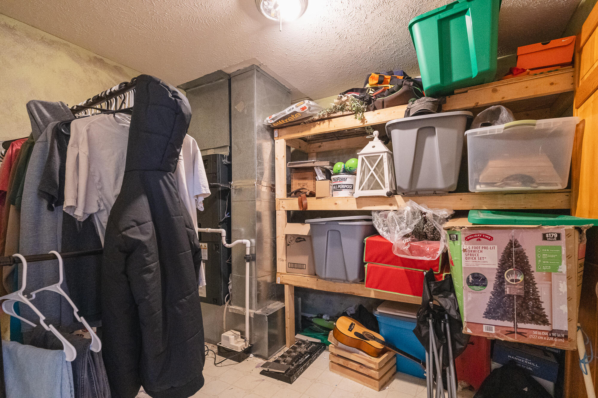 Basement storage area with crowded wooden shelves, a clothing rack, and a guitar on a crate.