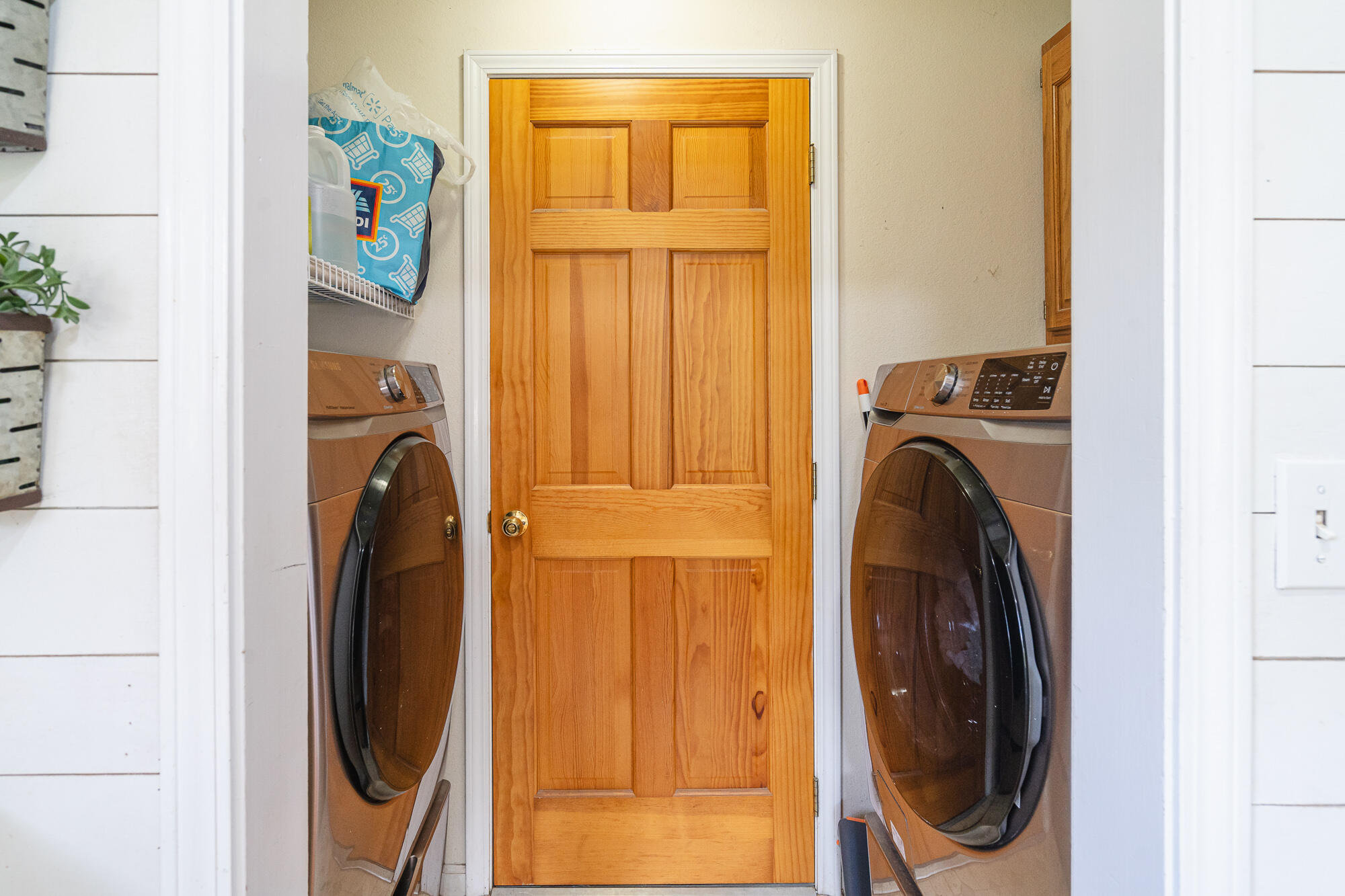 Laundry room with front-loading washer and dryer flanking a wooden paneled door.