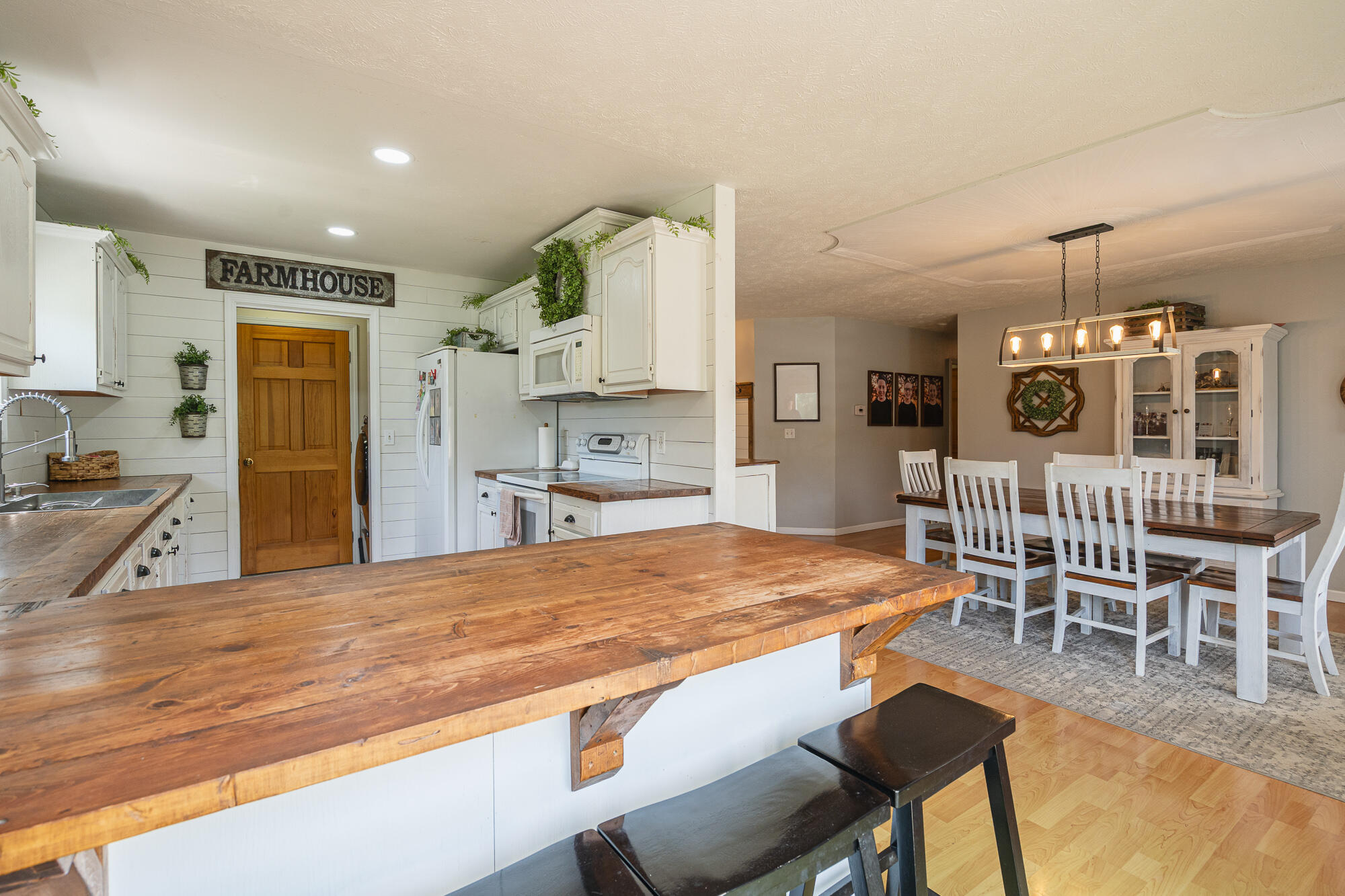 Farmhouse kitchen and dining area with a large wood island and white dining chairs.