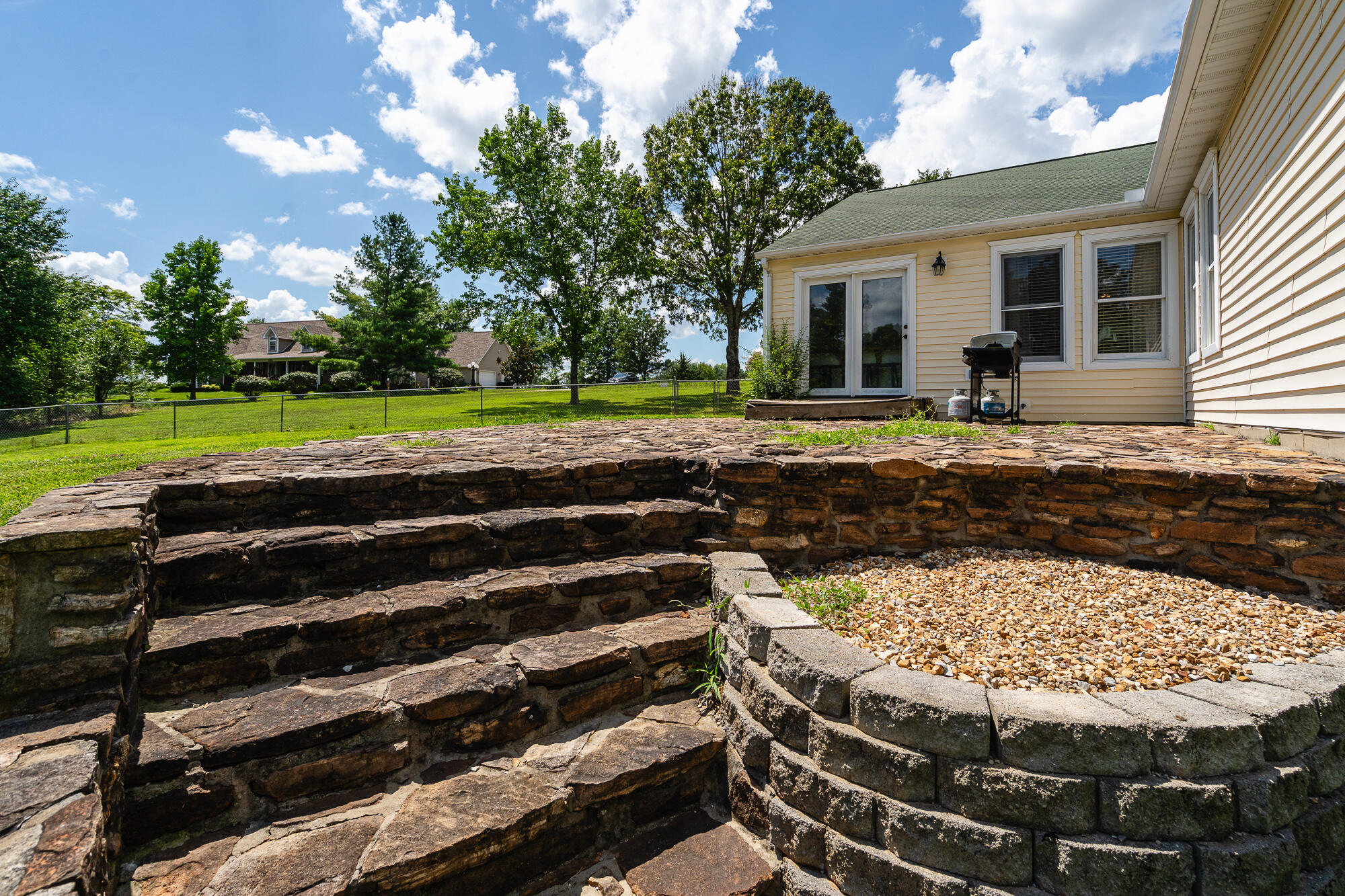 Backyard patio with broad stone retaining walls and steps around a gravel area beside the house.
