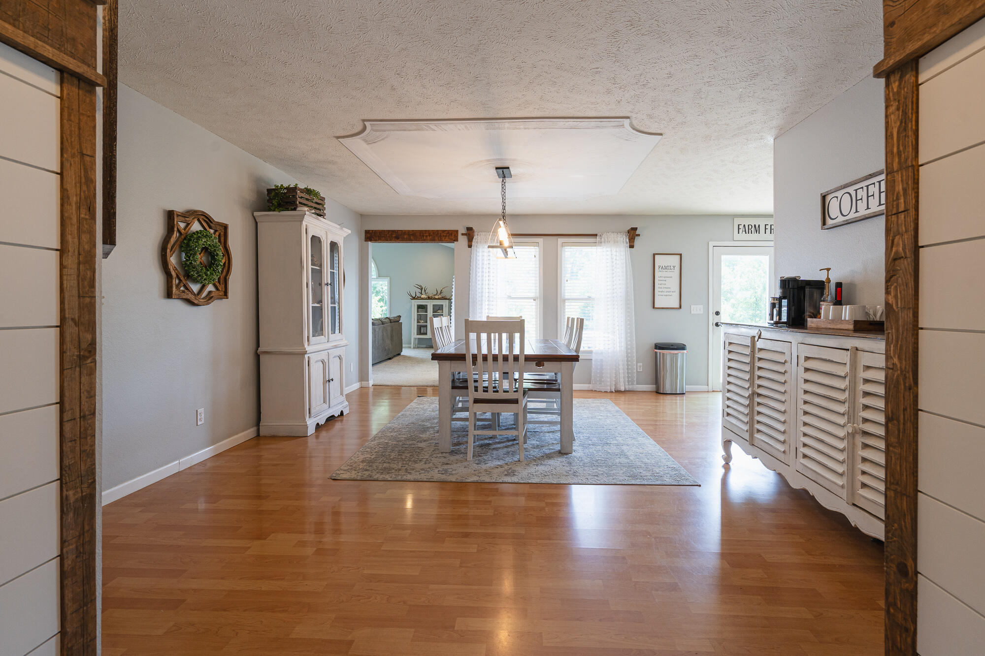Dining room with a wooden table, hardwood floors, bright windows, and a shutter-front sideboard.