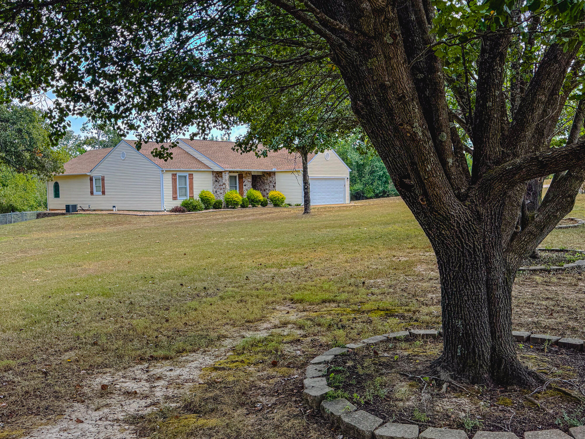 Single-story home with stone-accented entry and attached garage, framed by a large mature tree.